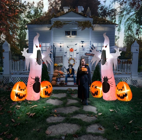 Person standing in front of a house decorated for Halloween with inflatable ghosts and pumpkins.