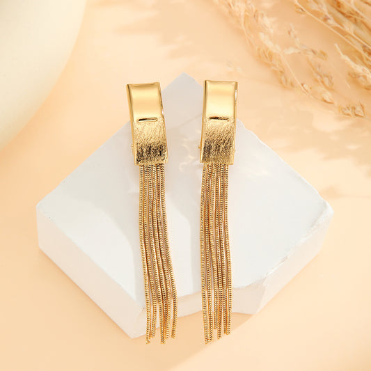 Gold fringe earrings on a white square with a beige background